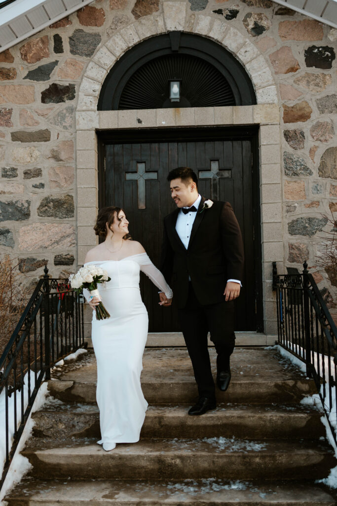 bride and groom walking down front steps of little stone chapel